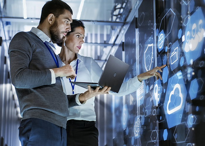 Two People Staring At Digital Screen Whilst Man Holds Laptop